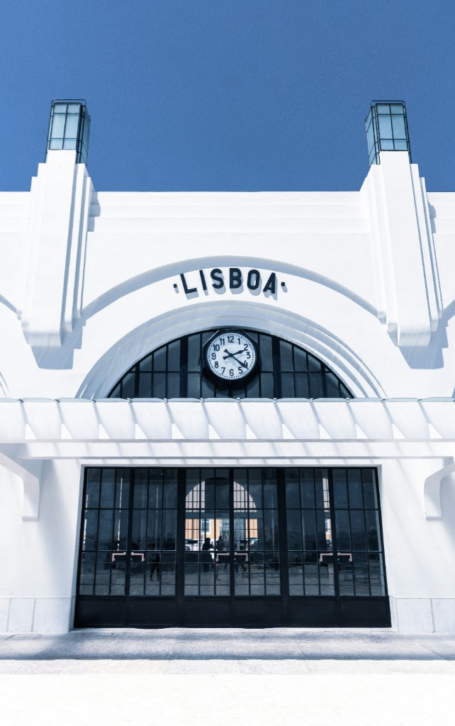 Santa Apolonia station facade in Lisbon, with LISBOA lettering, a clock, and twin towers against a clear blue sky