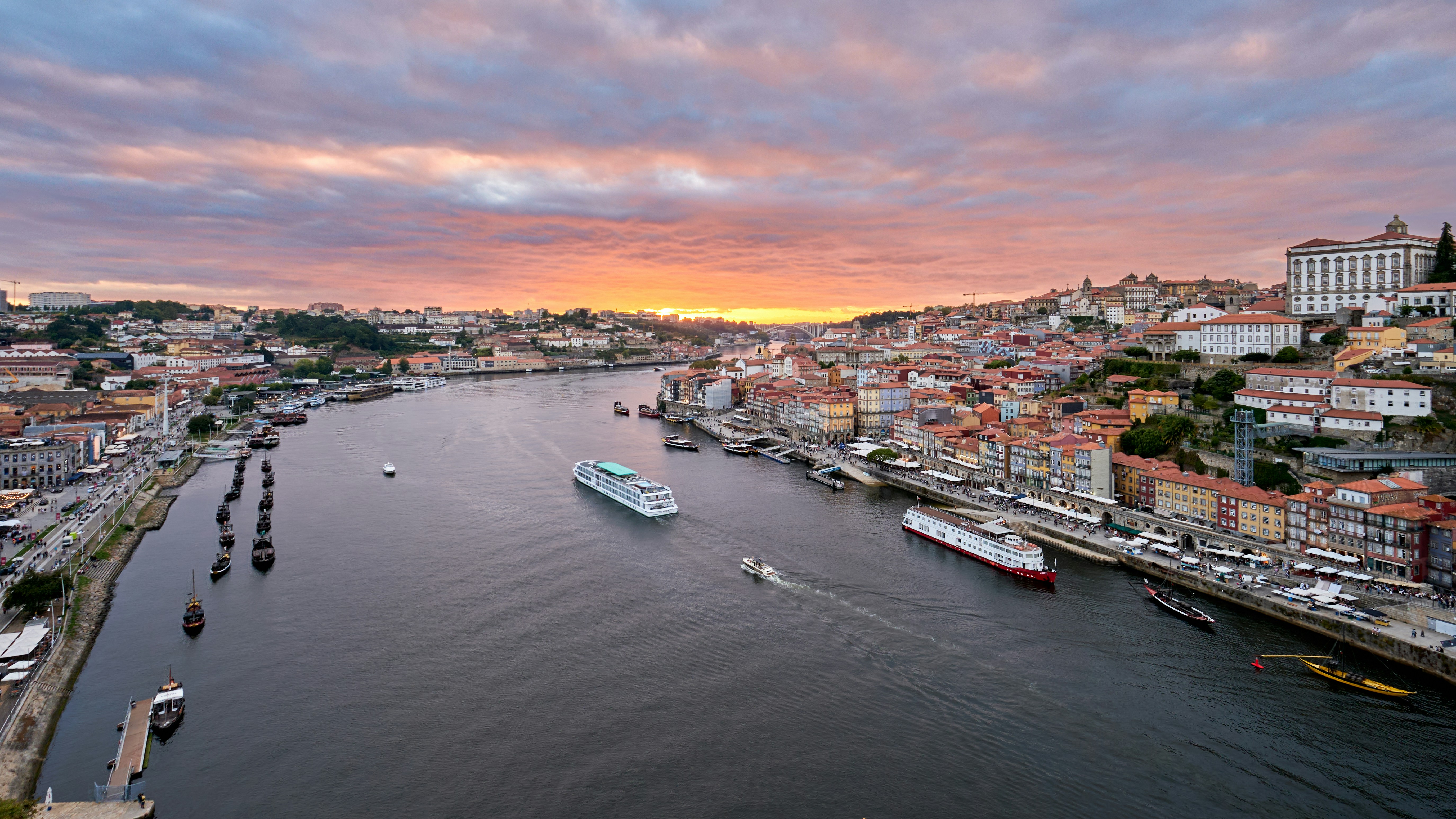 Aerial view of Porto’s Douro riverfront at sunset, with cruise boats on the water and terracotta-roofed houses along Ribeira