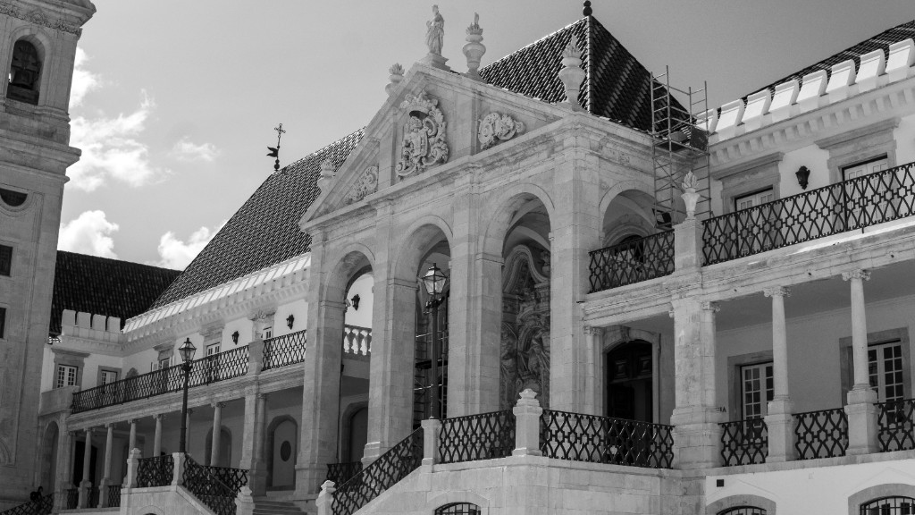 Black-and-white view of a stone building with a tiled roof, carved pediment, arched openings, iron balconies, and scaffolding