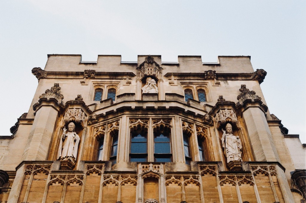 Limestone Gothic facade with standing statues in side niches, a sculpted group above the central window, and carved arches under a crenellated parapet
