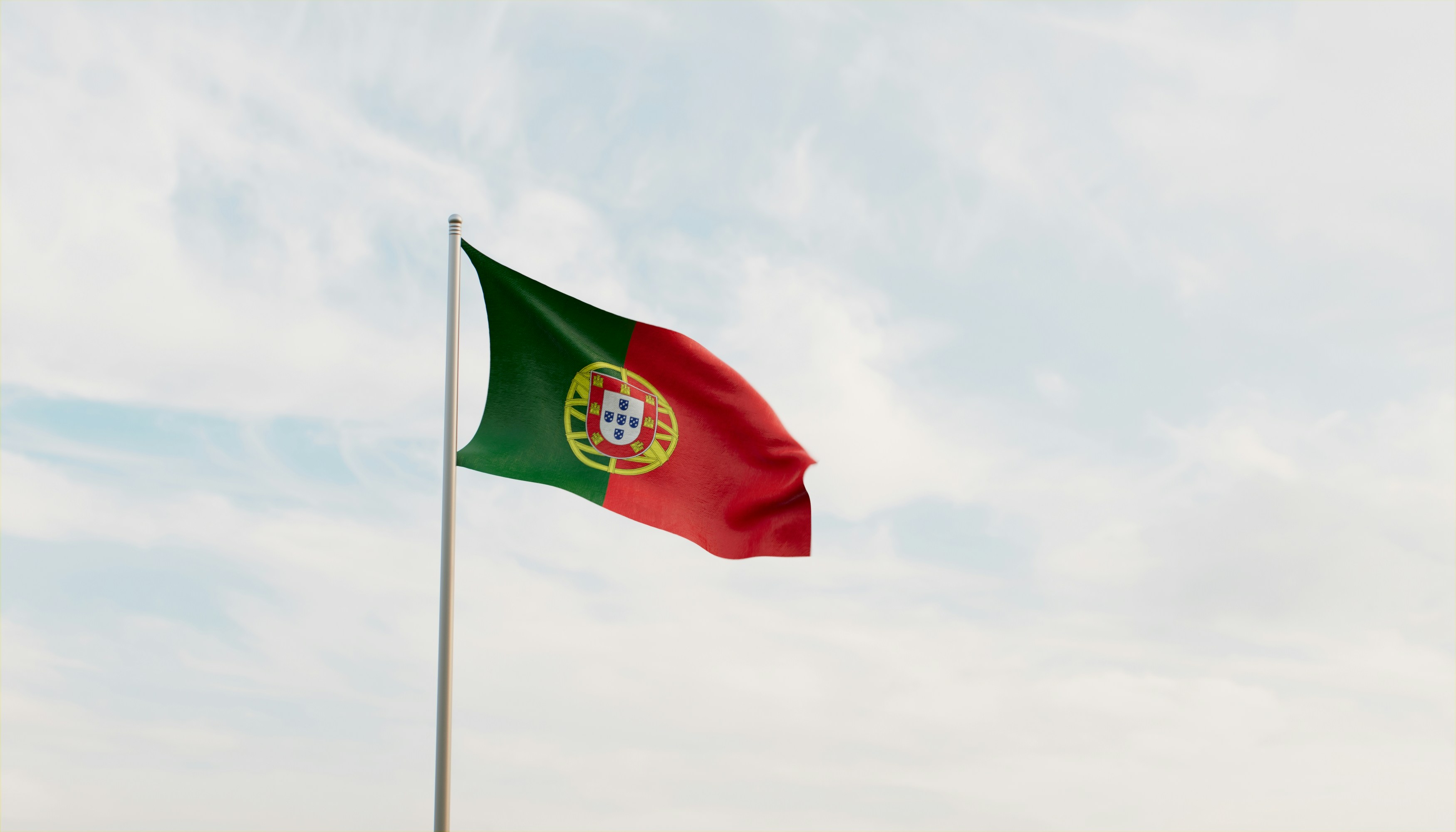 Portuguese flag on a silver pole against a pale, cloudy sky