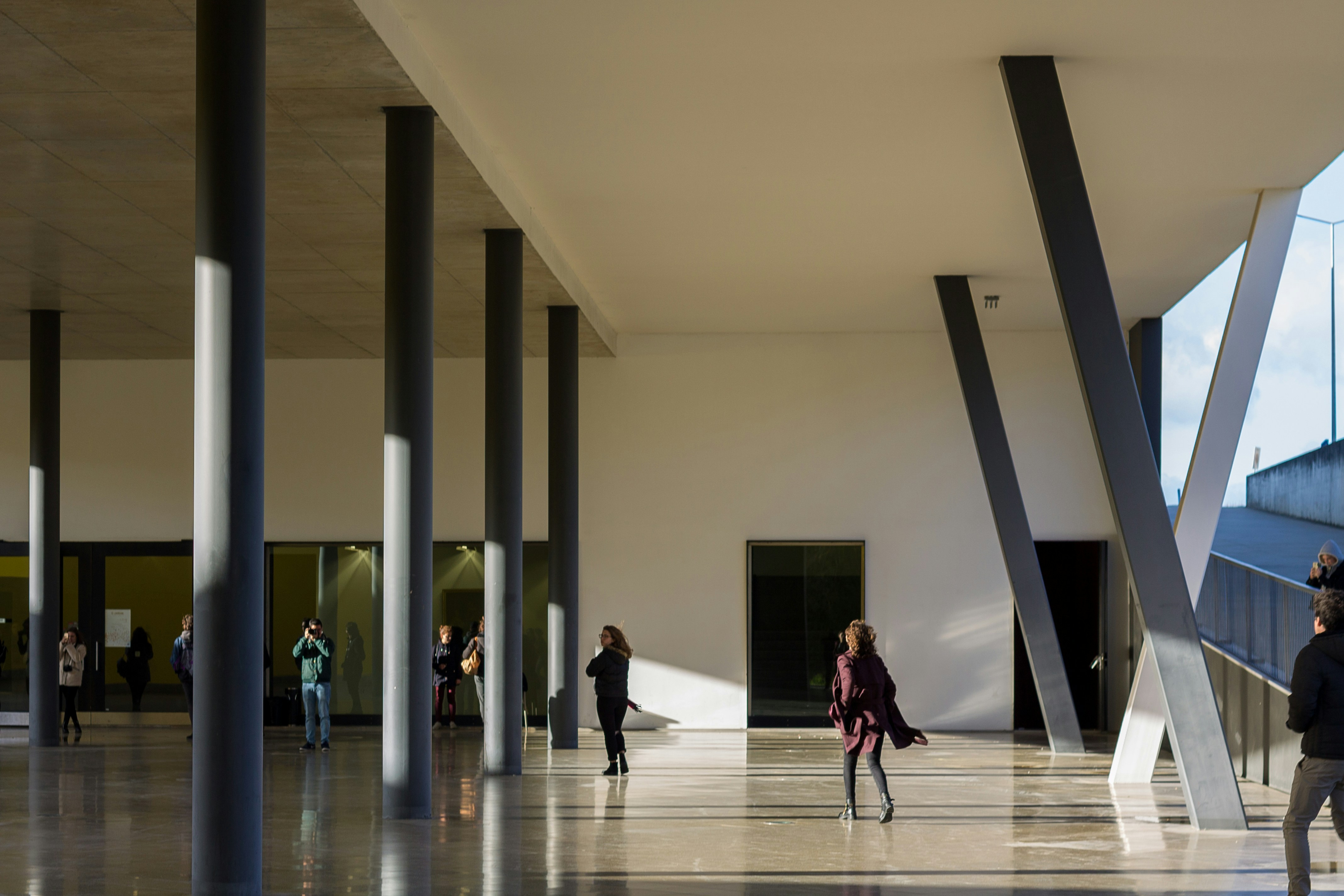 People walking through a tall colonnade with polished floors and angled steel supports