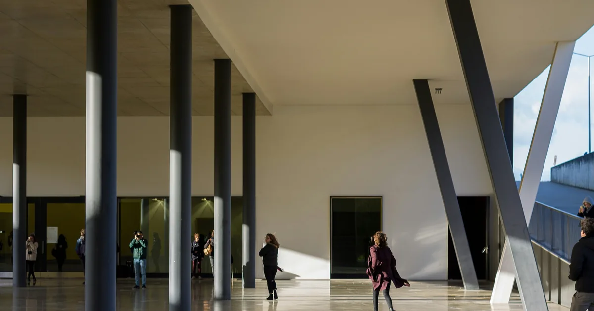 People walking through a tall colonnade with polished floors and angled steel supports