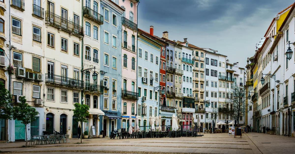 Lisbon square lined with pastel apartment buildings, cafe tables, and a cloudy sky