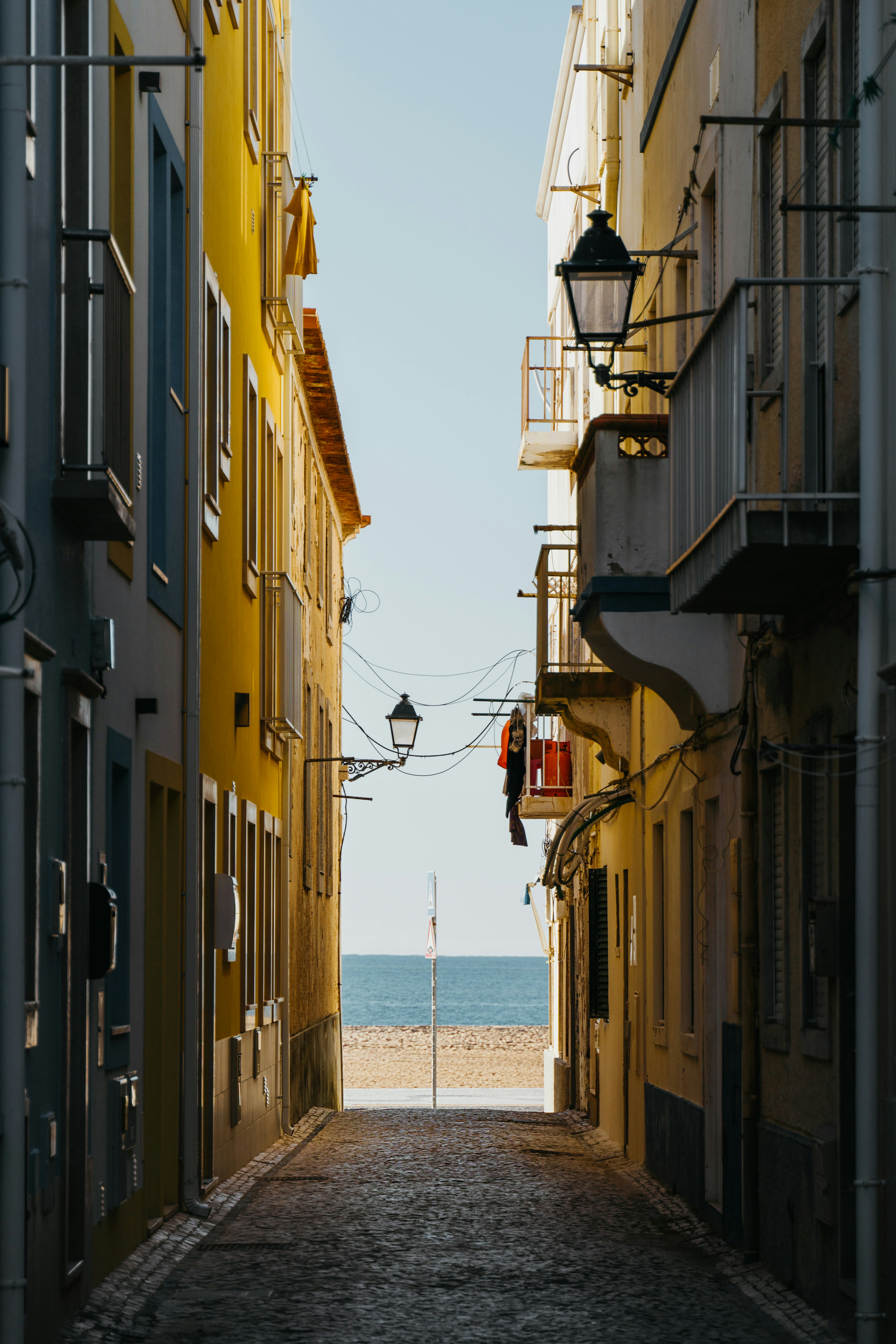 Narrow cobbled lane between yellow and cream houses that opens onto a beach and the sea