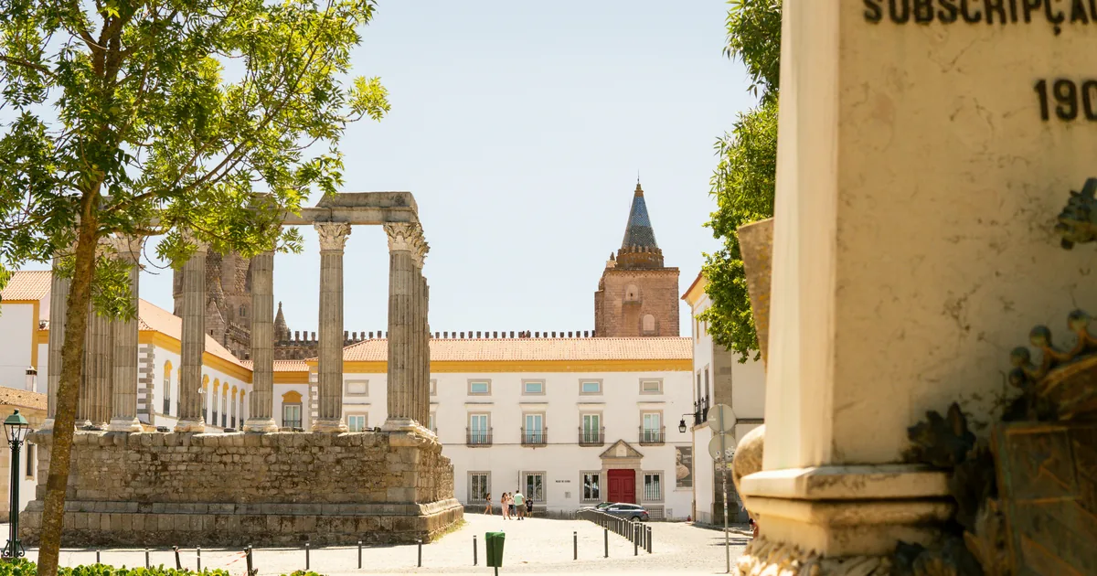 Roman temple columns in an Évora square facing a white palace and church tower