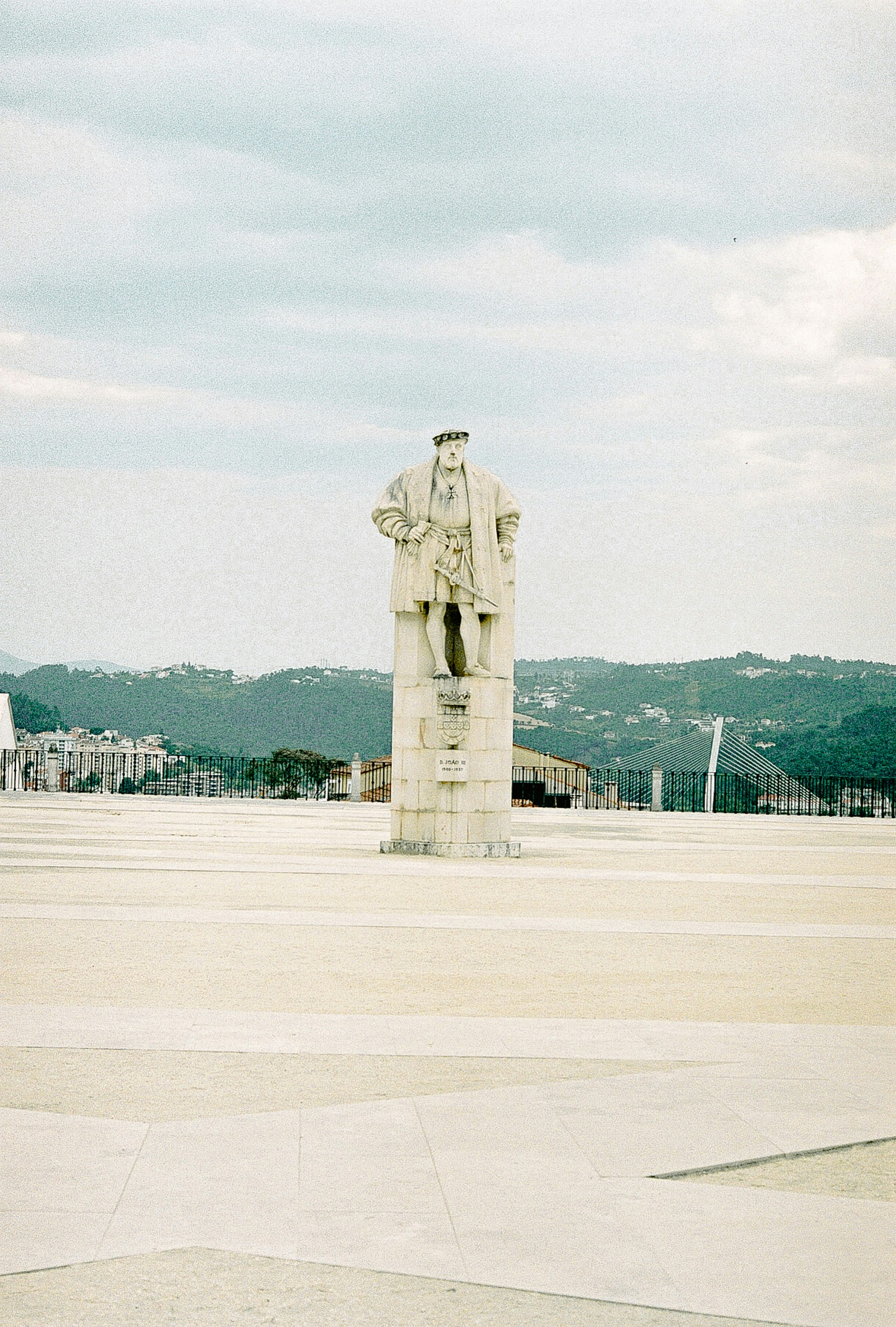 Stone statue of a man in sixteenth-century dress on a paved terrace, with hills and a cable-stayed bridge beyond