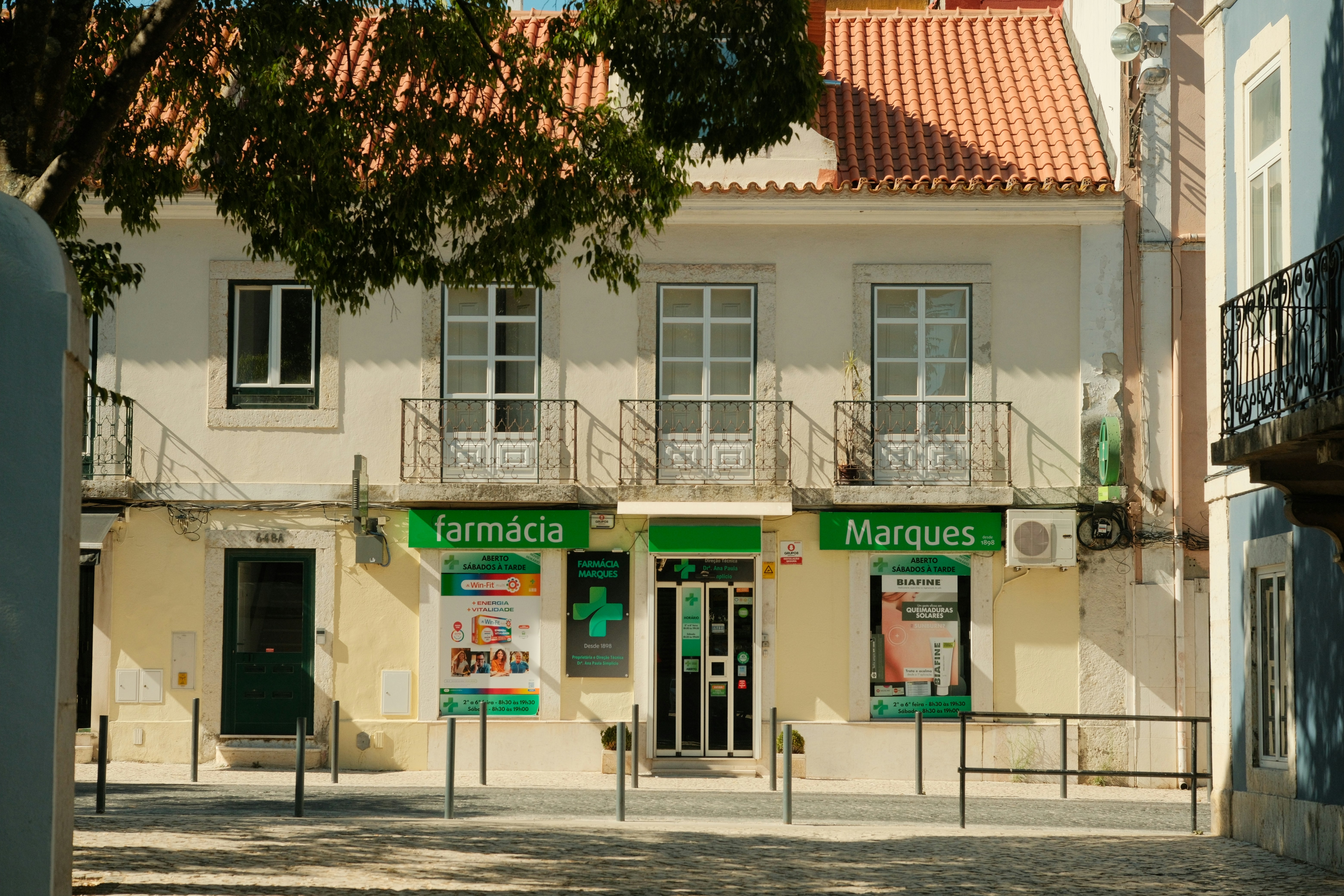 Street-level farmácia and Marques shopfront on a tiled Portuguese house with iron balconies