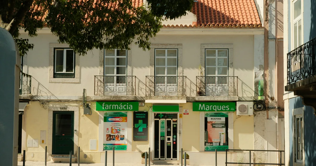 Street-level farmácia and shopfront on a tiled Portuguese house with iron balconies