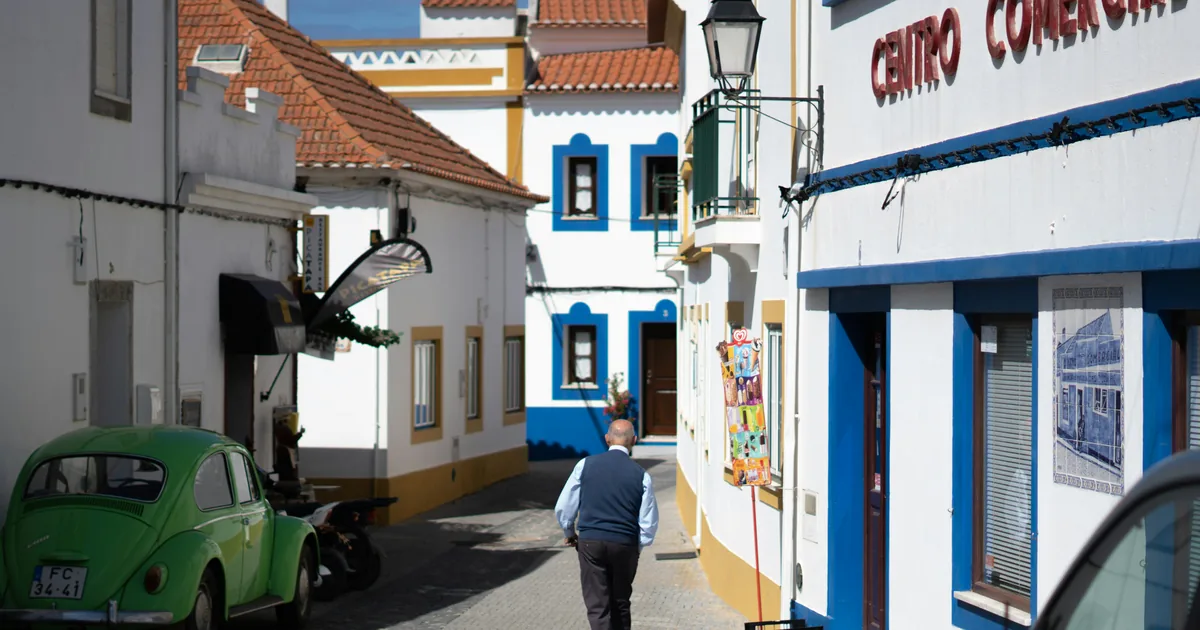 Man walking away down a cobbled lane past a green Volkswagen Beetle