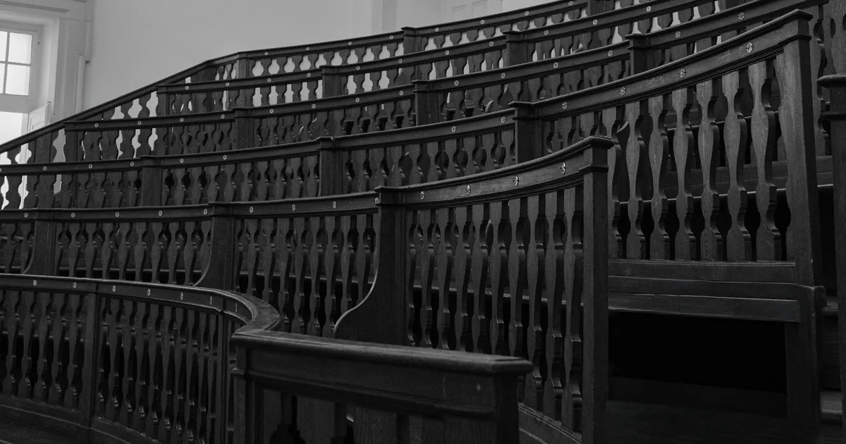 Empty dark wooden benches rising in a curved lecture hall with white walls