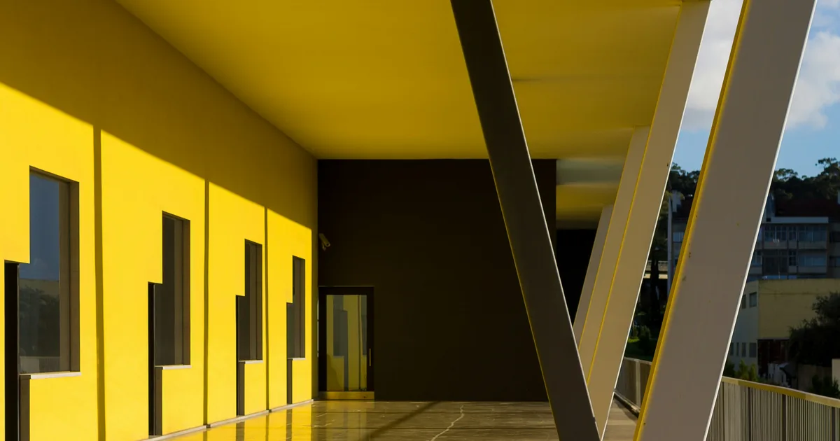 Yellow modern colonnade with dark windows and white diagonal steel beams