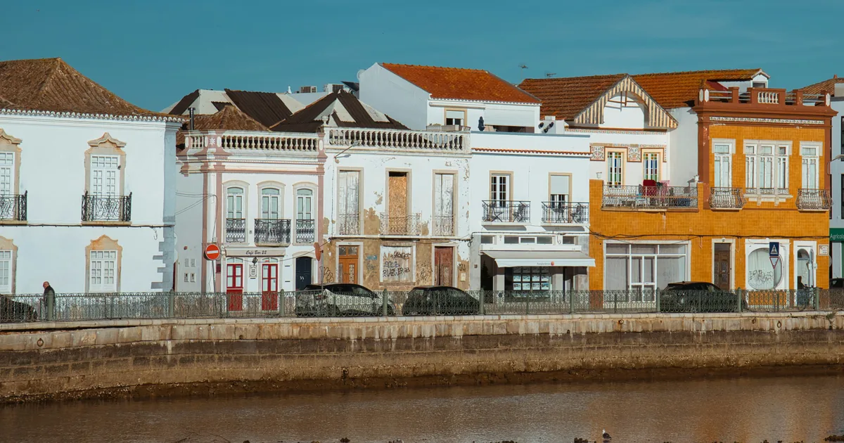 Row of white and ochre houses along a tidal mudflat, with parked cars and wading birds