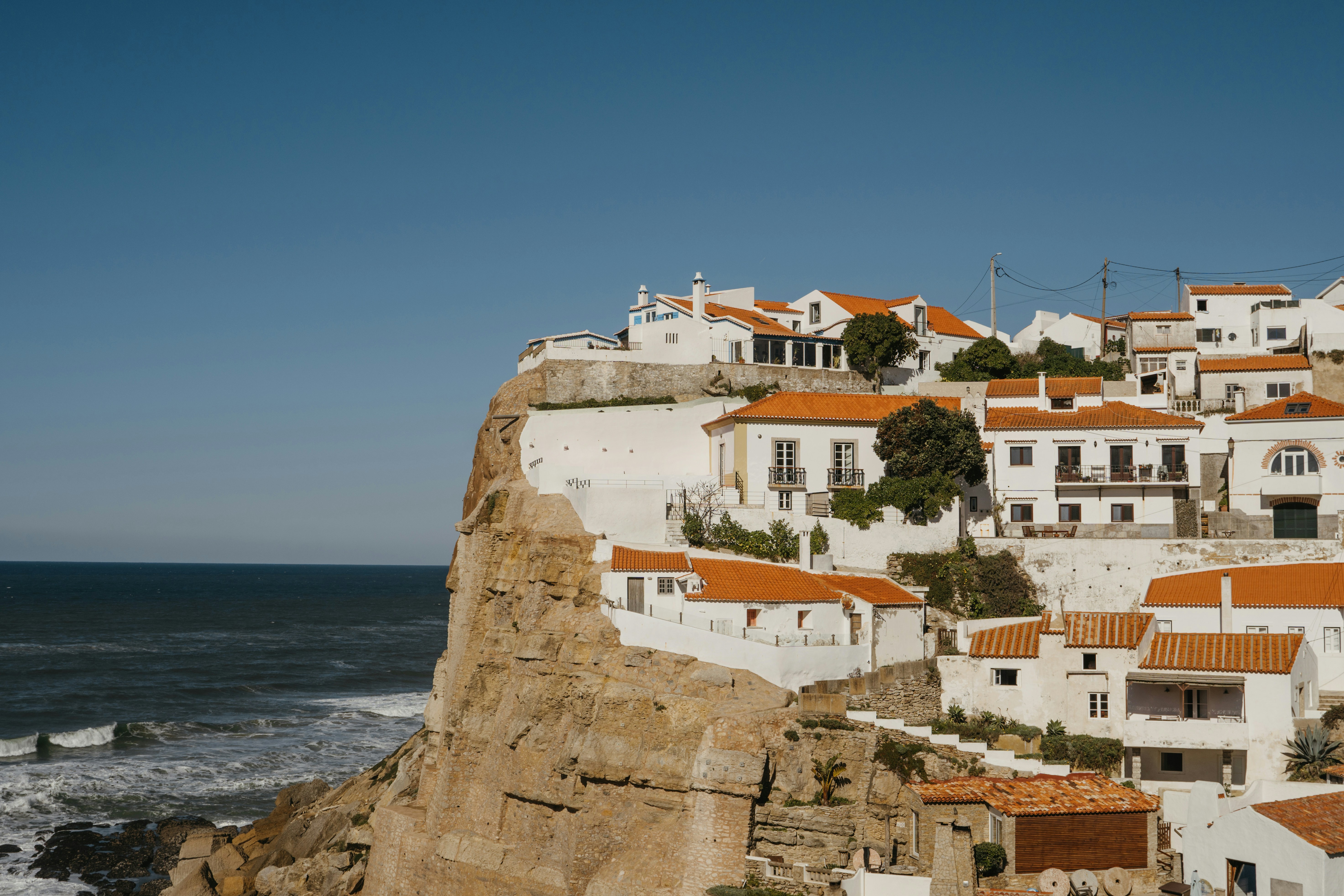 White houses with terracotta roofs stacked on a sea cliff above breaking waves