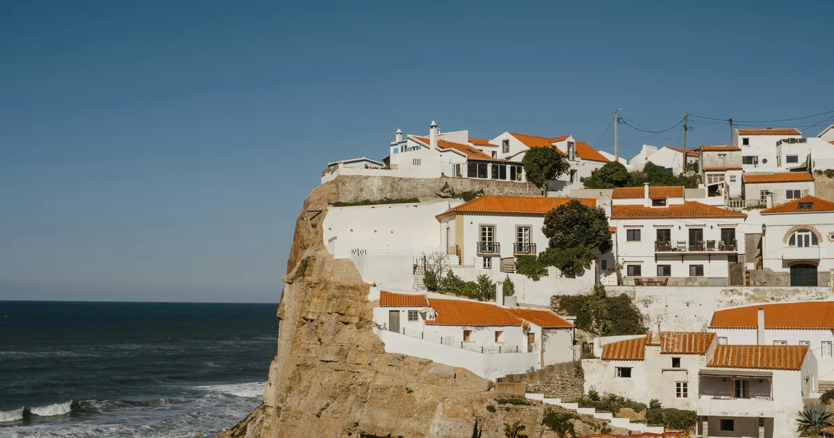 White houses with terracotta roofs stacked on a sea cliff above breaking waves