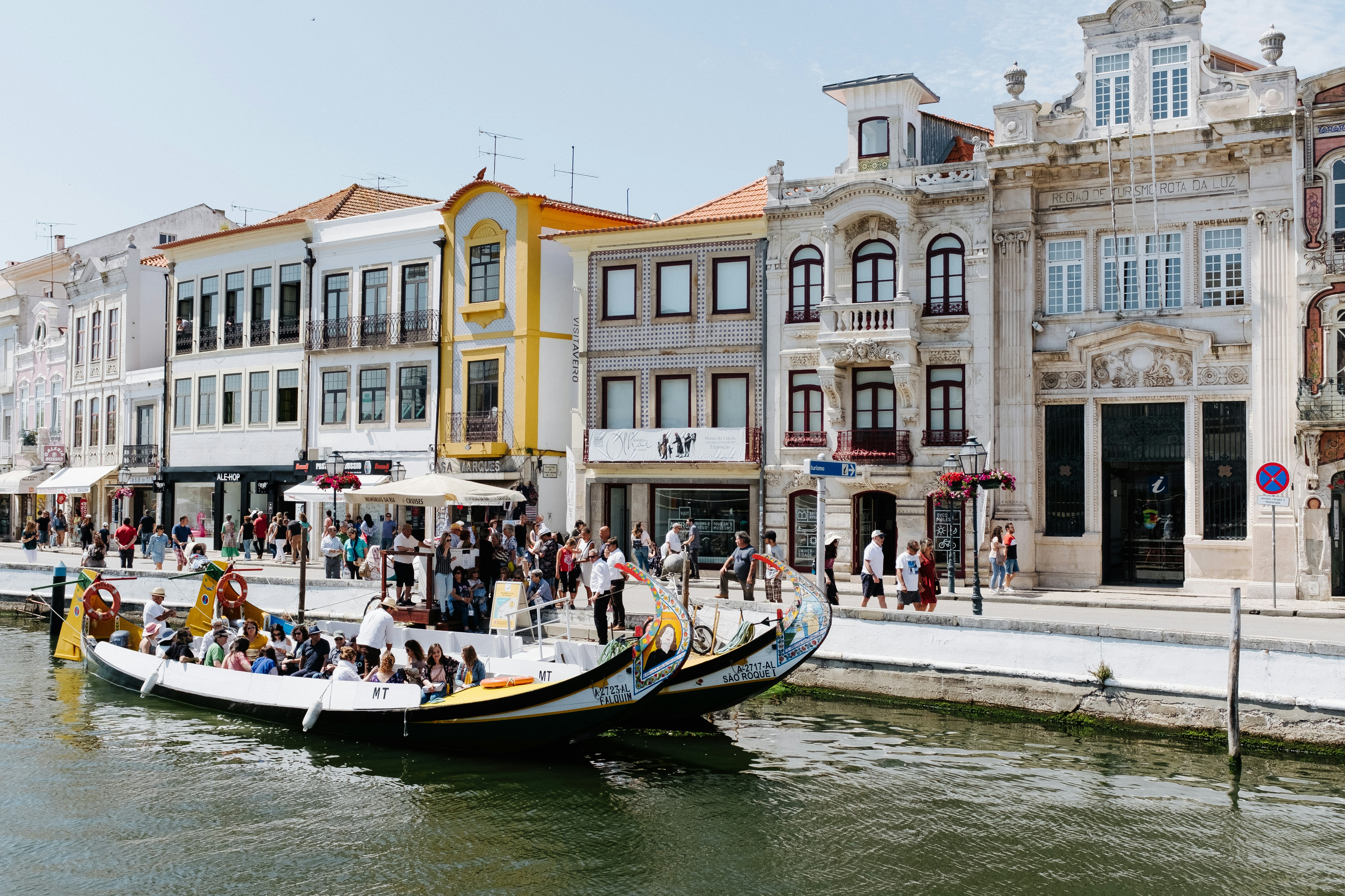 Moliceiro boats on the canal in Aveiro, with tiled facades and pedestrians on the quay