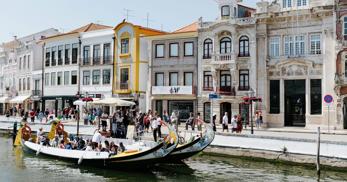 Moliceiro boats on the canal in Aveiro, with tiled facades and pedestrians on the quay