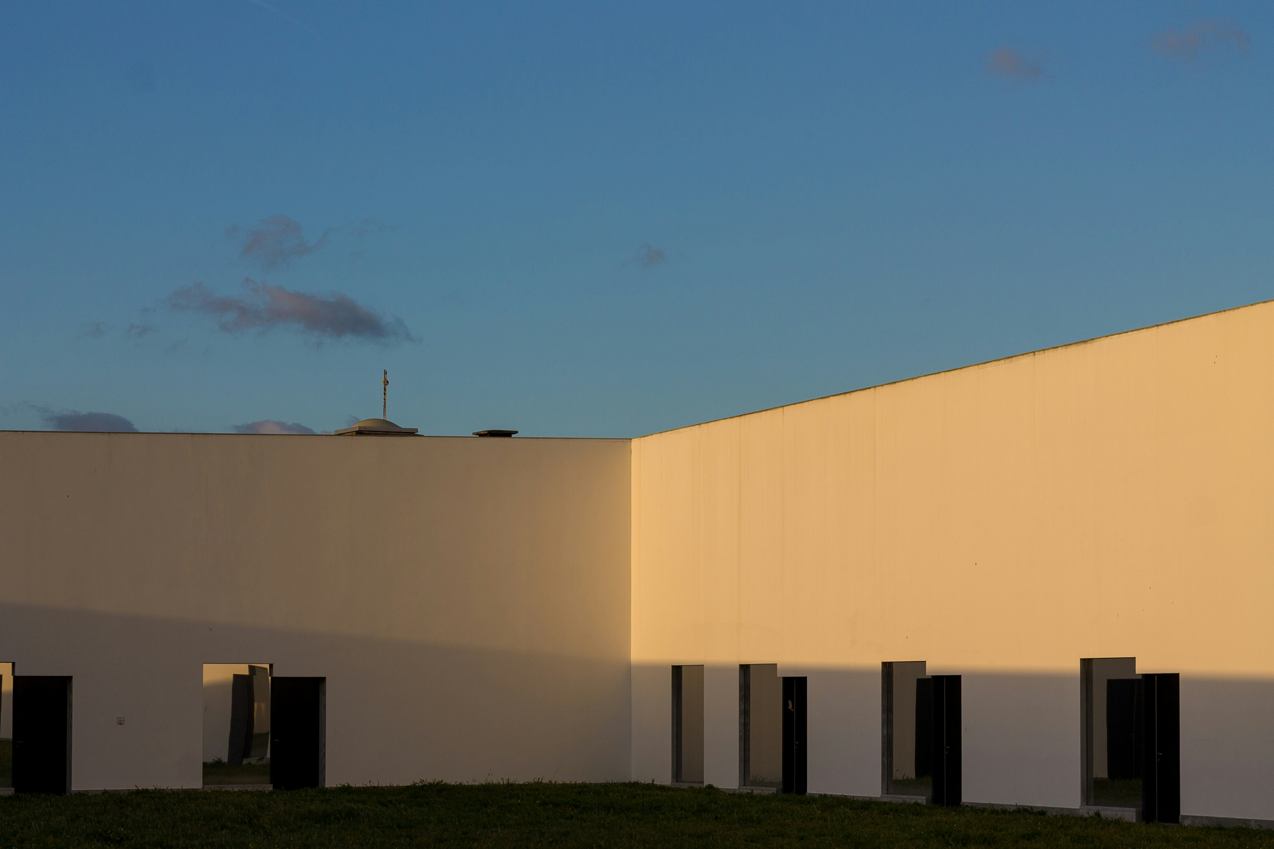 White modernist courtyard walls with dark door openings and a small dome catching late sun