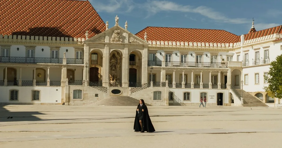 Historic university courtyard with terracotta roofs, a stone pediment, and a person in a black academic cape