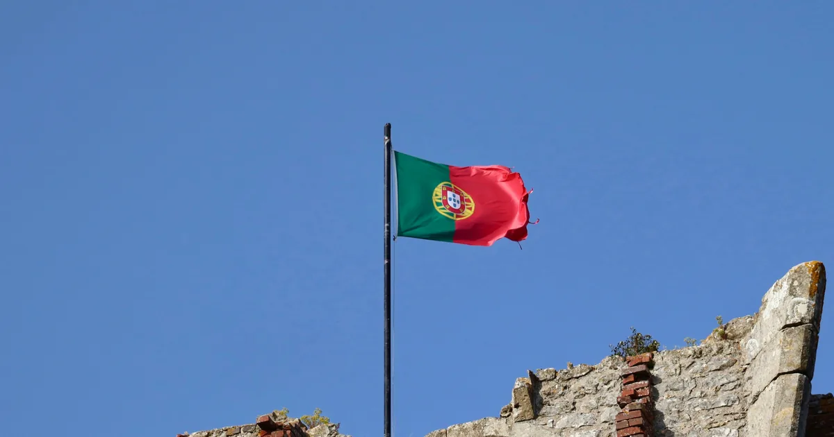 Portuguese flag on a black pole above a ruined stone wall