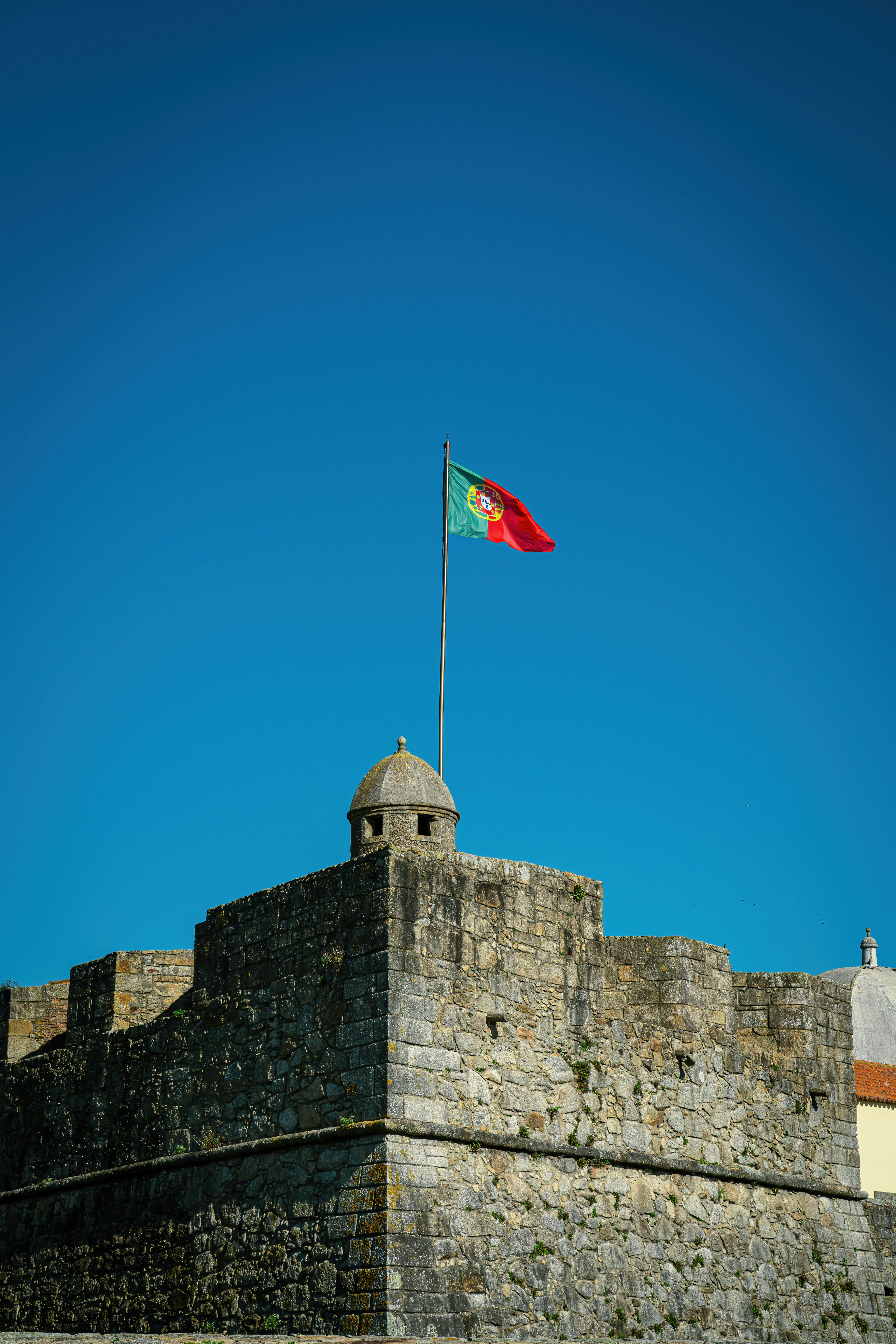 Portuguese flag on a stone fortress corner turret against a deep blue sky