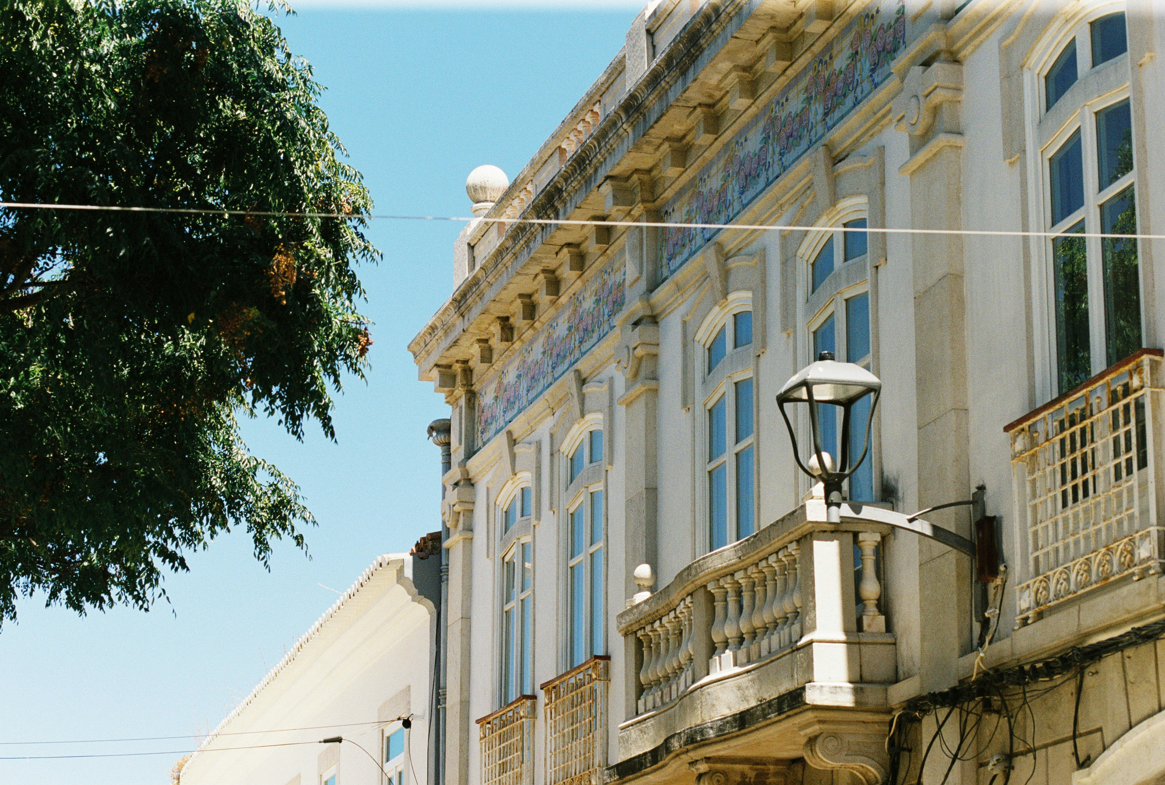 Cream facade with tiled lettering, stone balconies, and a black lantern against a bright sky