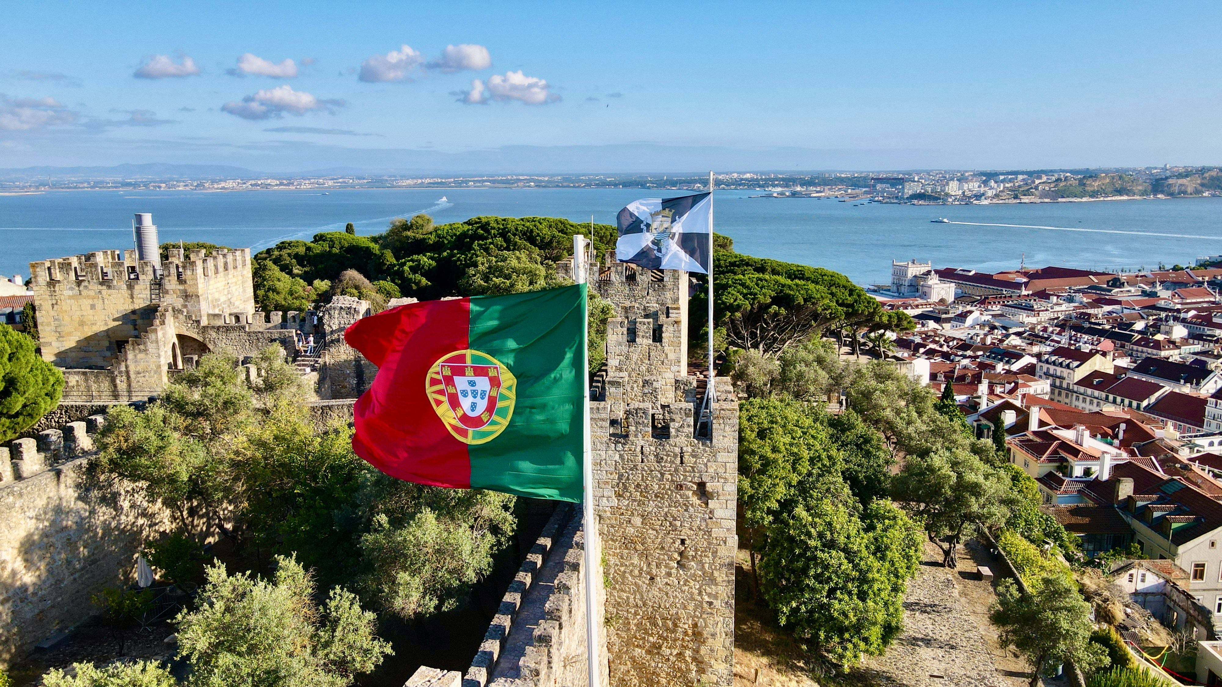 Portuguese and Lisbon flags on São Jorge castle walls, looking over the Tagus and the city’s red roofs
