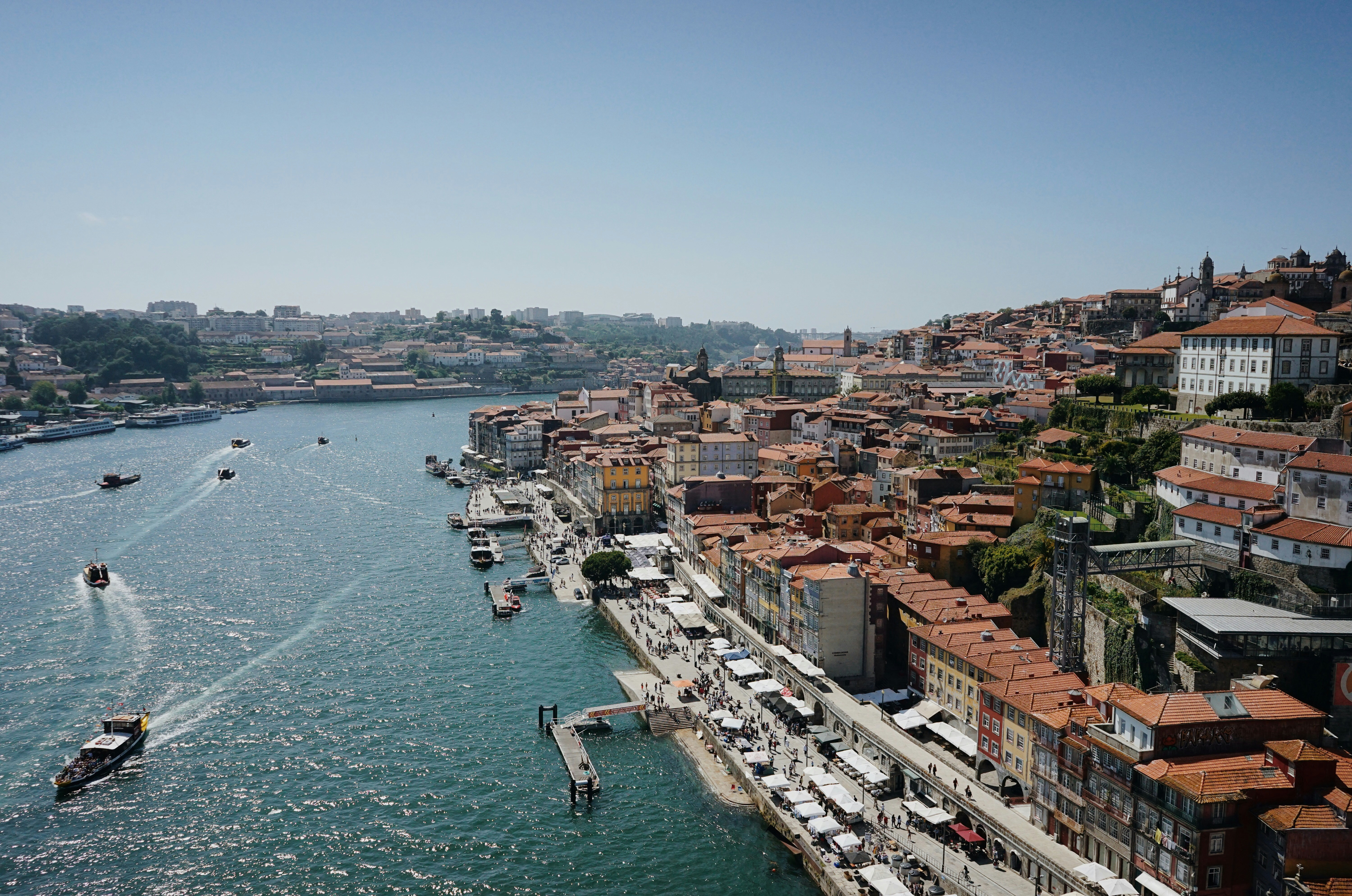 Sunlit Ribeira waterfront in Porto, with boats on the Douro and packed terracotta roofs climbing the hillside