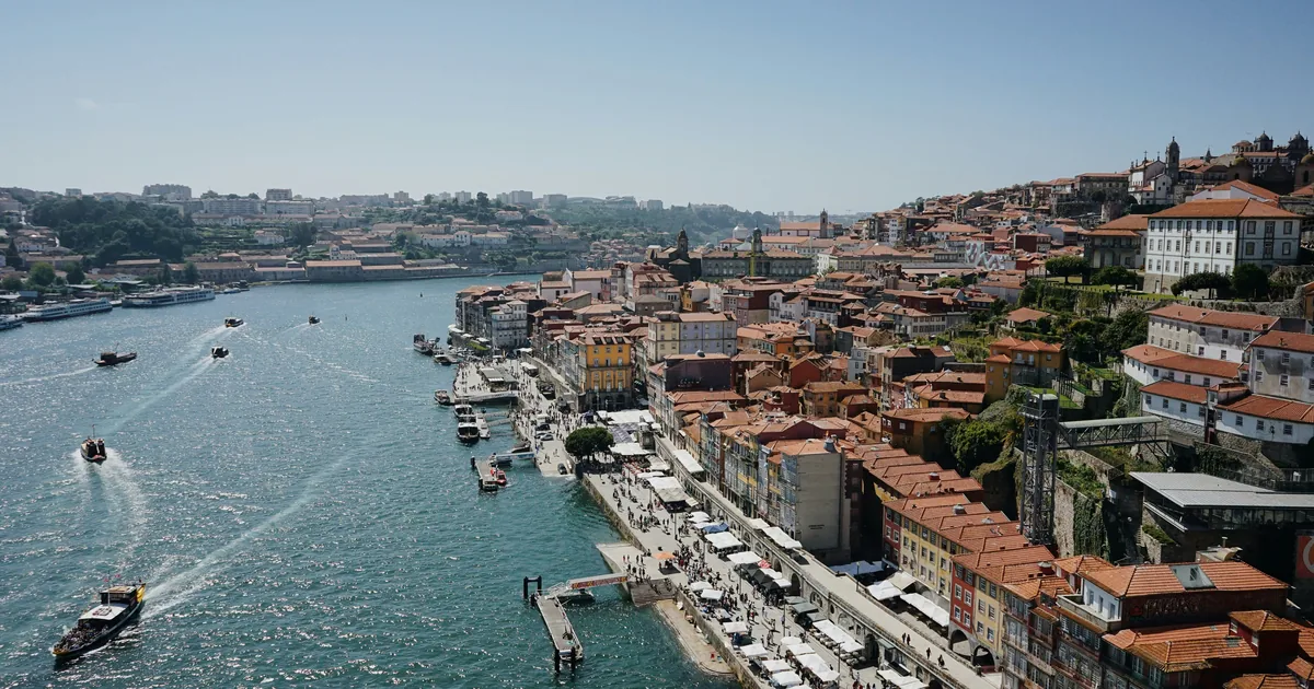 Sunlit Ribeira waterfront in Porto, with boats on the Douro and packed terracotta roofs